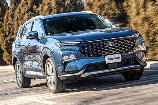 Dynamic action shot of a metallic blue Ford Territory compact family SUV driving along a tree-lined highway.