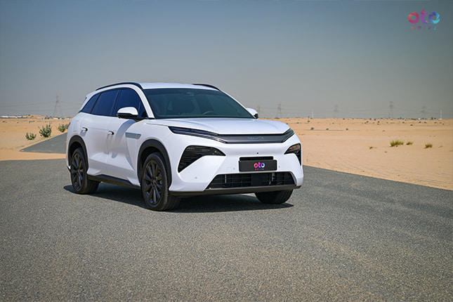 Side front view of a premium white XPENG G9 electric crossover SUV driving on an open desert highway road.