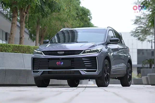 Sleek gray Geely Coolray SUV parked outdoors on a modern city street, surrounded by greenery and urban architecture, conveying a sense of style and sophistication.