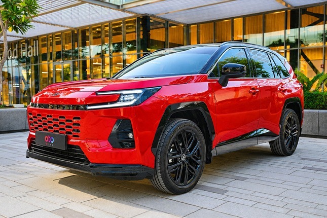 Front angle view of a sleek red Toyota RAV4 Hybrid SUV parked outside a modern commercial glass building.