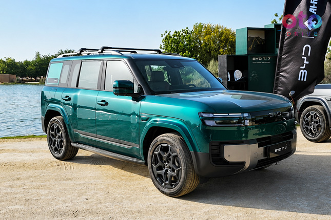 Front three-quarter view of a teal green BYD Bao 5 off-road SUV parked near a body of water.