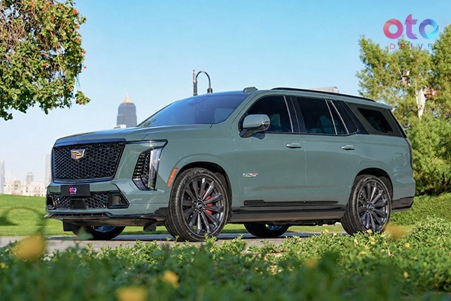 Front three-quarter profile of a dark green Cadillac Escalade V luxury SUV parked on grass.