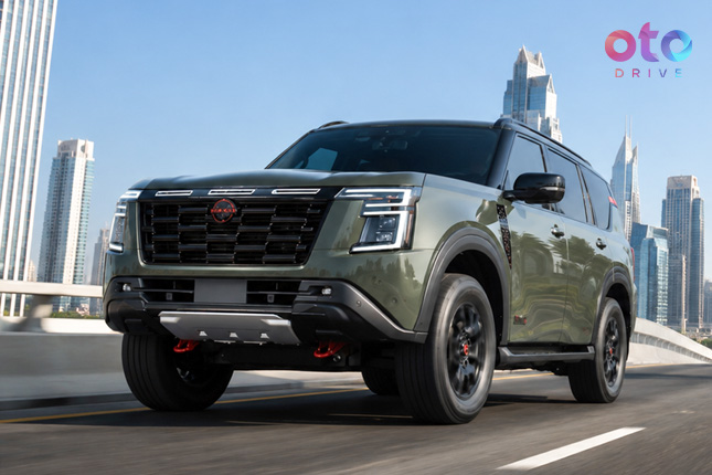 Front three-quarter view of an olive green Nissan Patrol SUV driving on an urban highway with skyline.