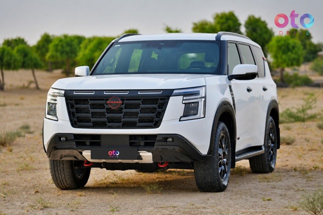 Front three-quarter view of a white Nissan Patrol SUV with red accents parked on a sandy desert track.