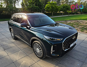A side-angle view of a dark green Chery Tiggo 9 SUV parked on a paved outdoor courtyard under the sun.